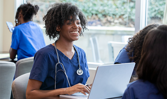 physician smiling and using laptop while others work in background.